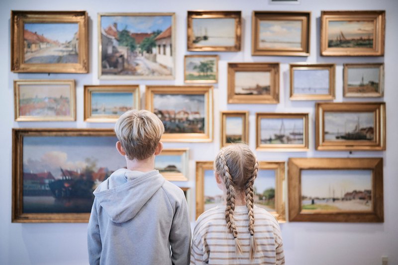 To børn kigger på en væg med en masse ophængte billeder med massive rammer