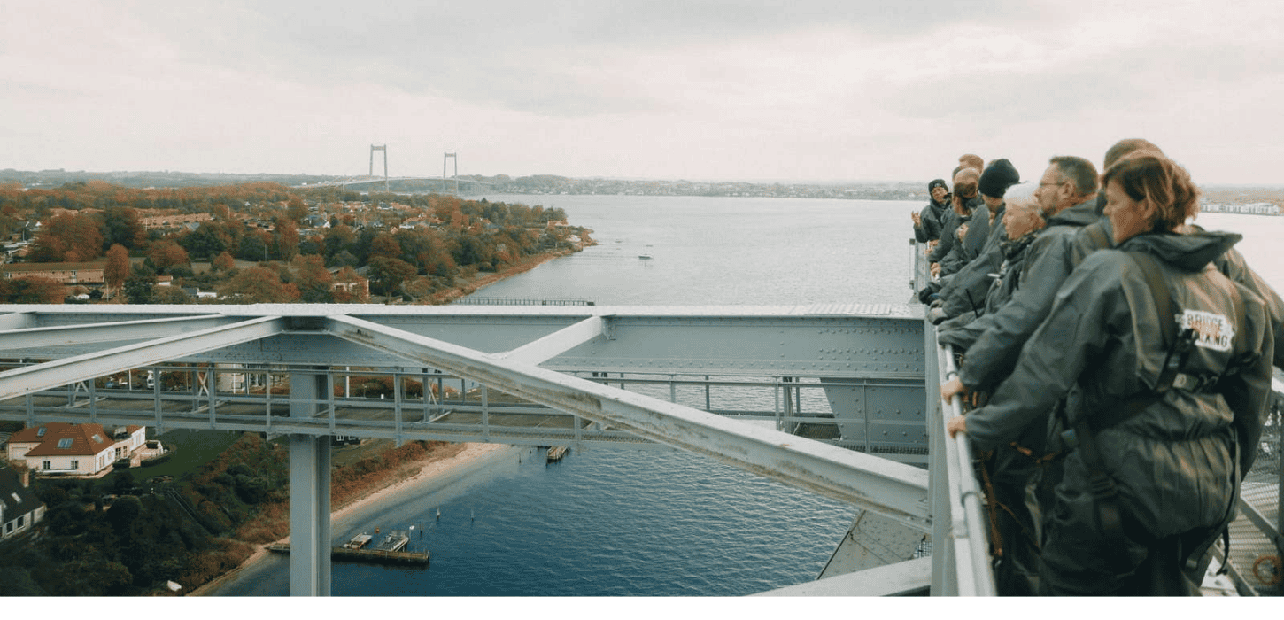 En gruppe mennesker står på en bro højt oppe med udsigt til hav og land med den Nye Lillebæltsbro i baggrunden