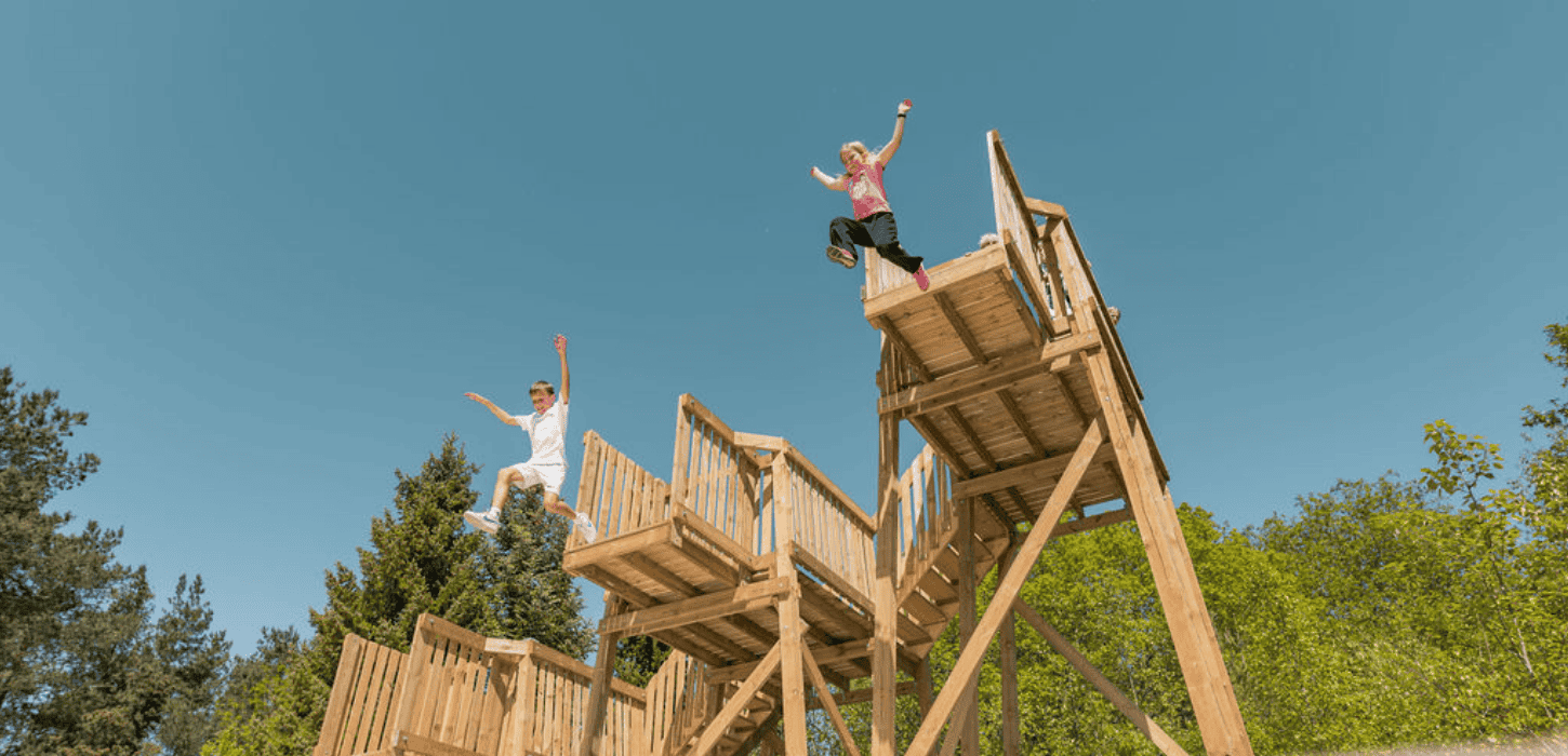 To børn hopper ud fra to trætårne 