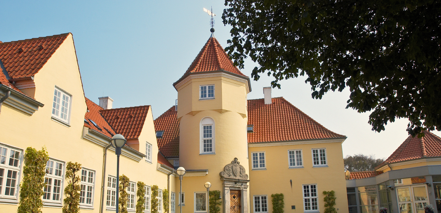 Et gult hotel med rødt tegltag og et tårn