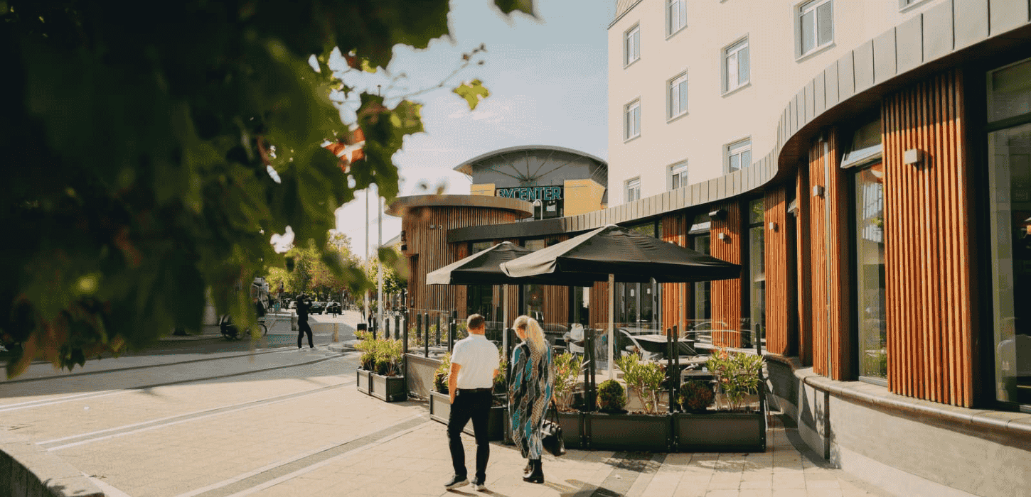 En træbelagt facade ud til et torv, hvor der går en mand og kvinde
