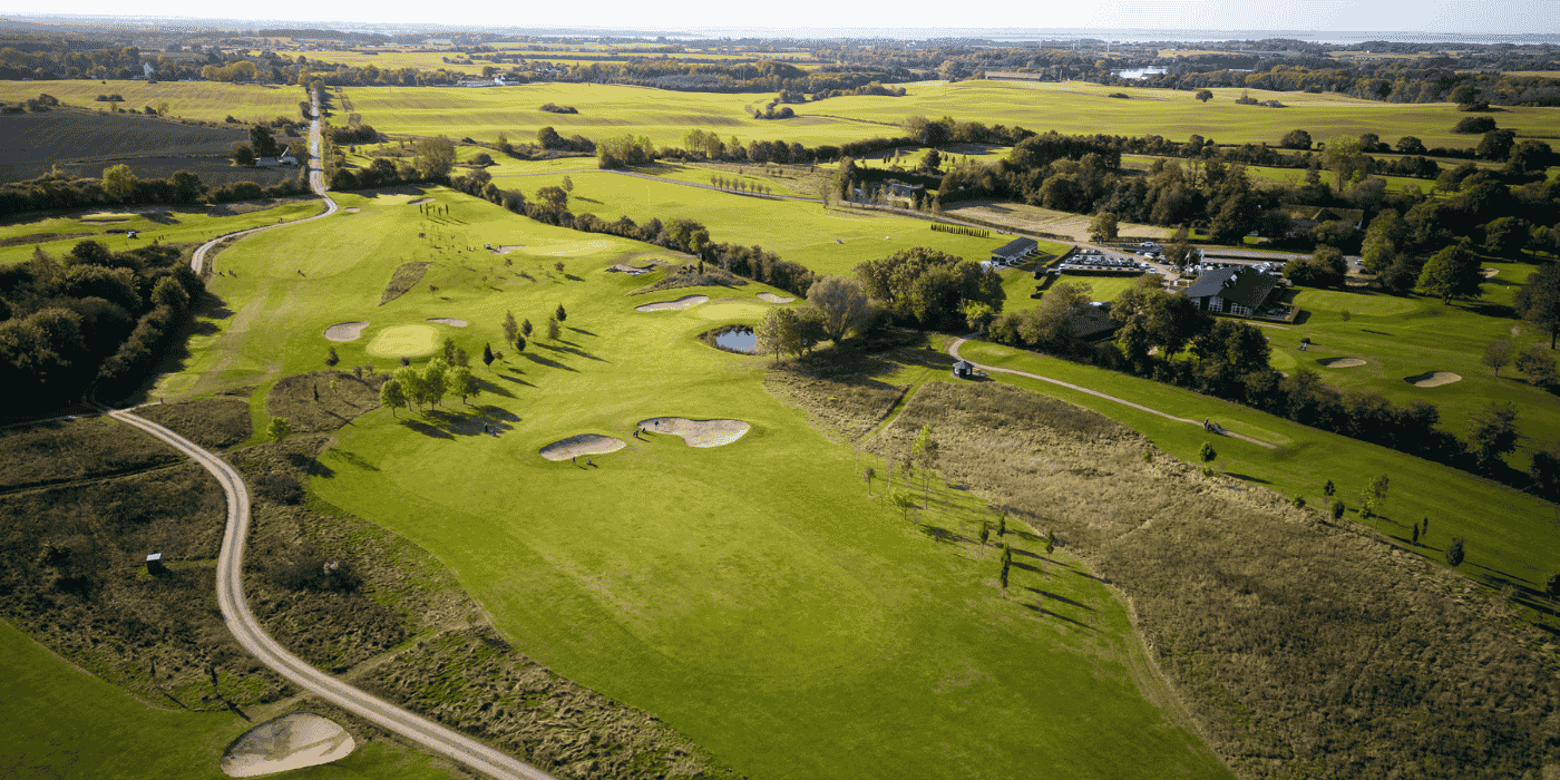Luftfoto af golfbane med træer, stier og bunkers. 