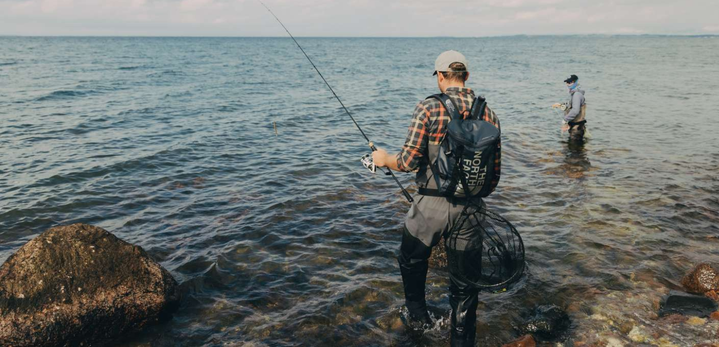 To lystfiskeri iklædt outdoortøj og waders står i havet med fiskestænger