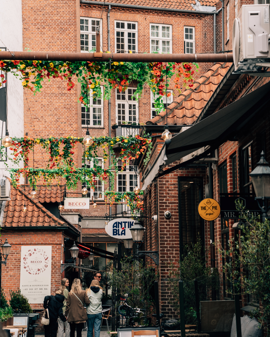 Et dekoreret stræde med skilte, røde facader og mennesker, der går
