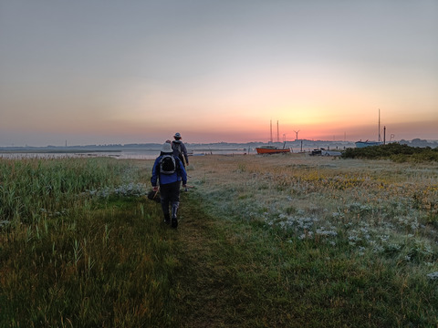 To personer bevæger sig langs en sandbelagt sti mod havet i enten solop- eller nedgang