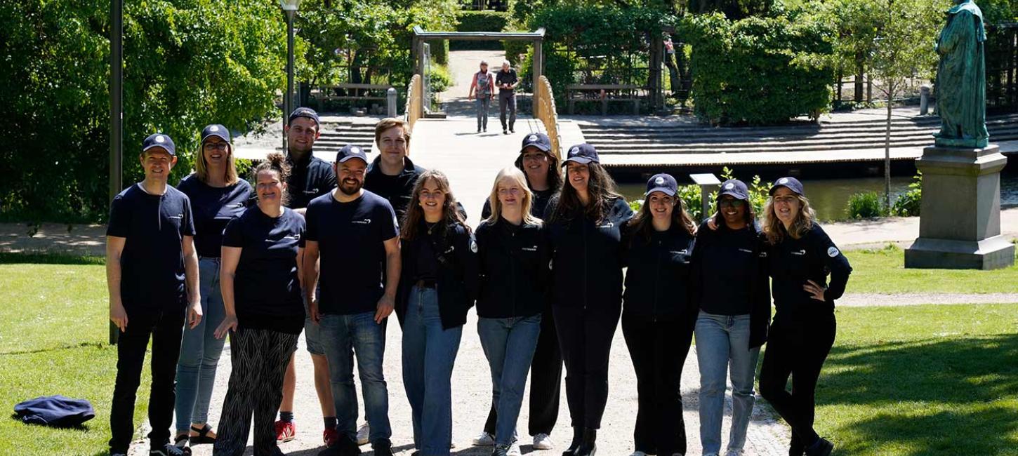 En gruppe turistguides i mørkeblåt tøj og kasketter står og smiler til kameraet.