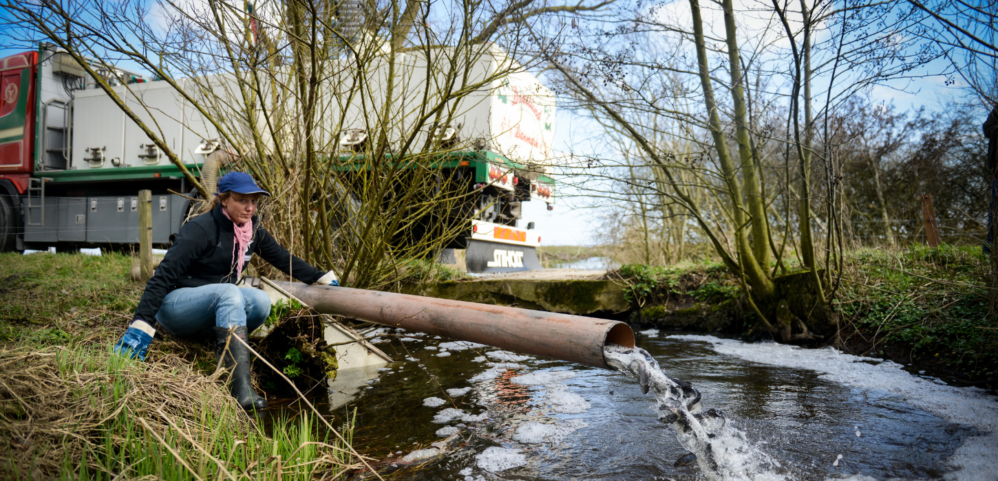 Kvinde sidder ved rør, der vælter vand og smolt ud af og ned i en å.