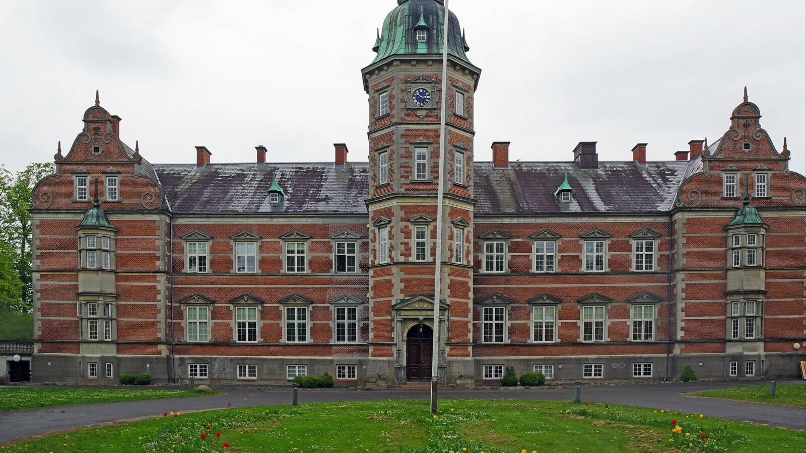 Flot rød herregård med sort tag og et stort tårn i midten.