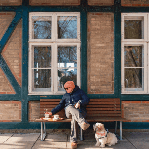 En kvinde iført vintertøj sidder ude foran en kaffebar med sin hund i snor og kaffe på en bakke