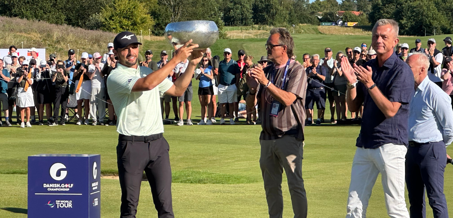 Golfspiller løfter stort trofæ, og folk omkring ham klapper