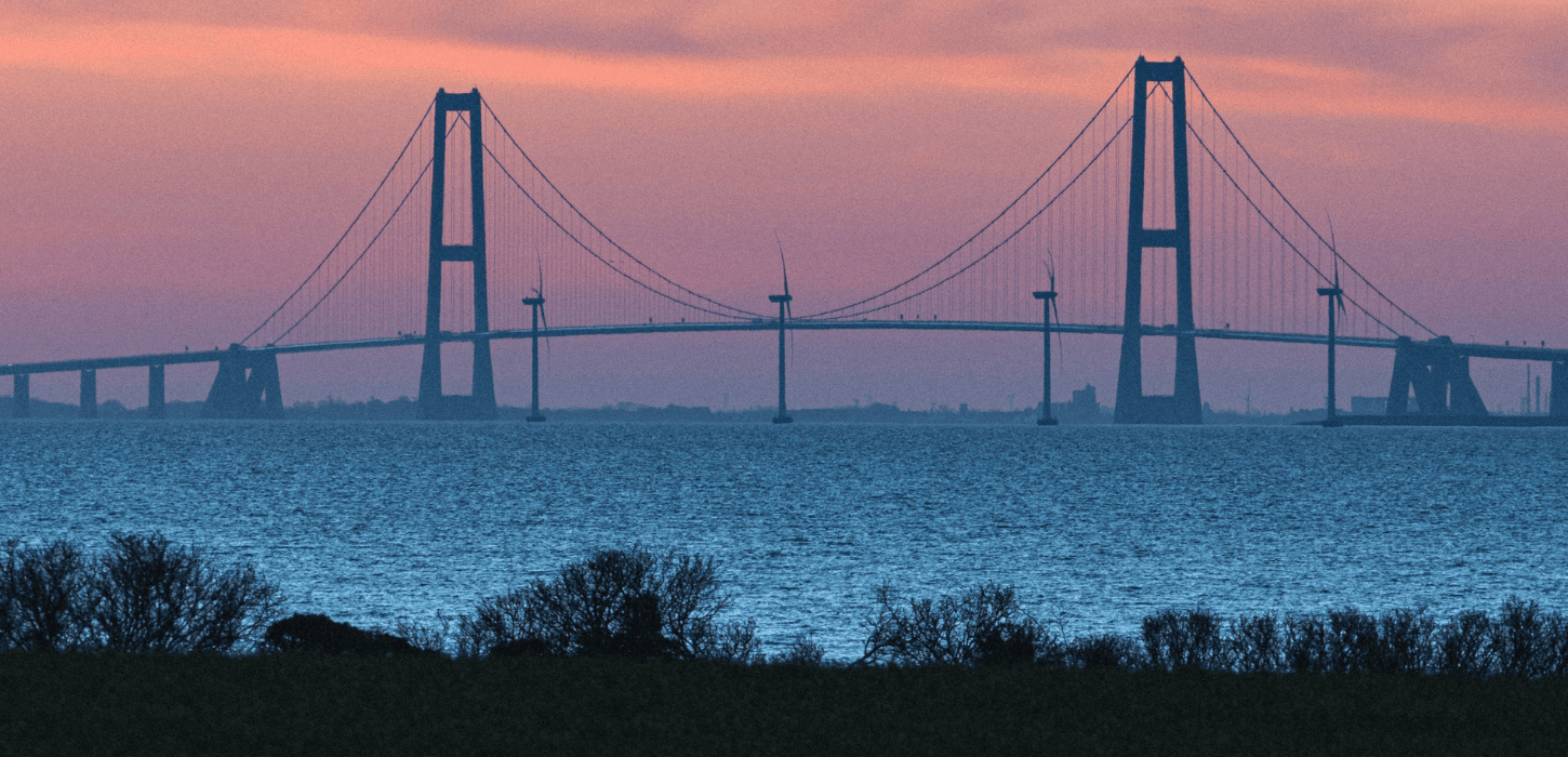 Storebæltsbroen i solnedgang, der forbinder Fyn og Sjælland over et stille vand.
