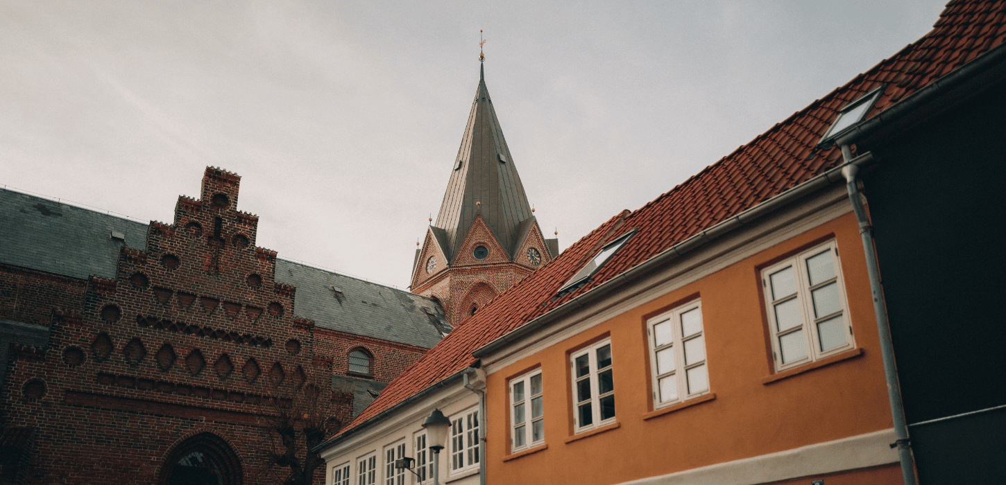 Et billede af tre forskellige bygningers tage og øverste dele, heriblandt et kirketårn