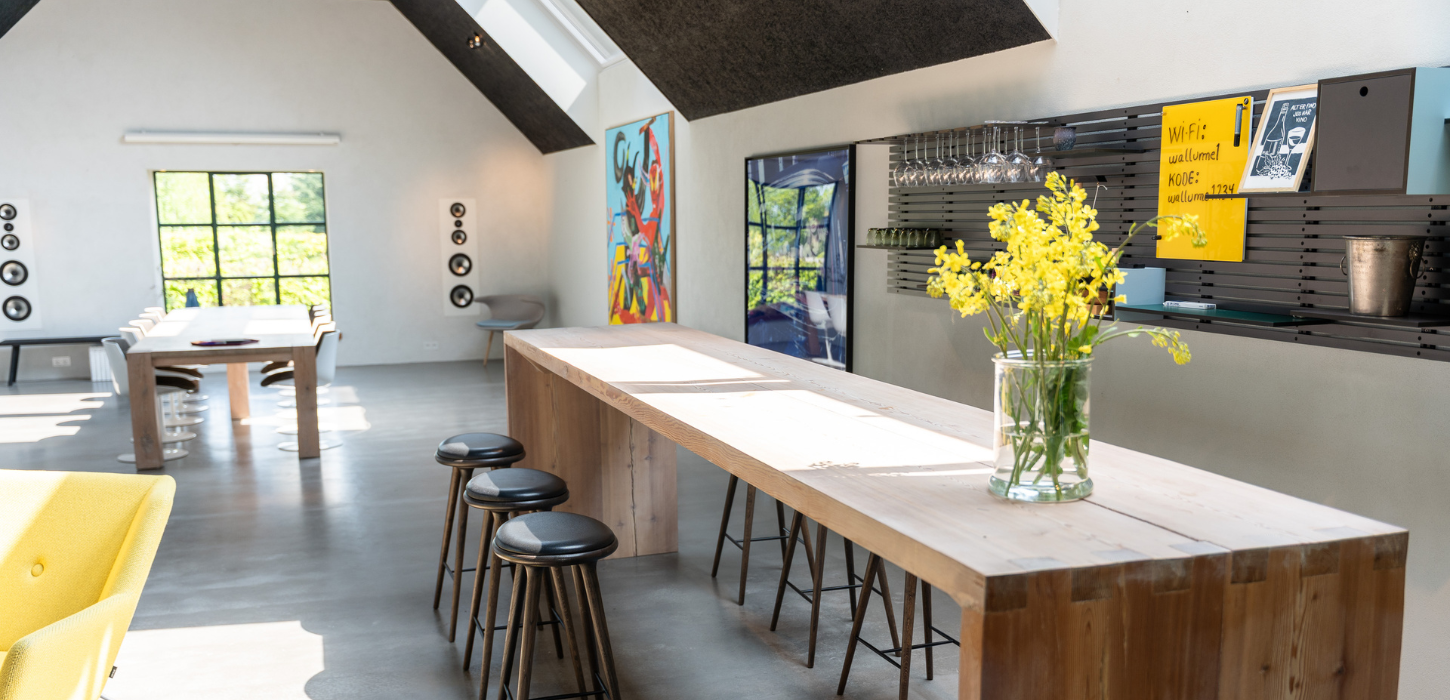 Lyst mødelokale med højt plankebord og barstole og et mødebord