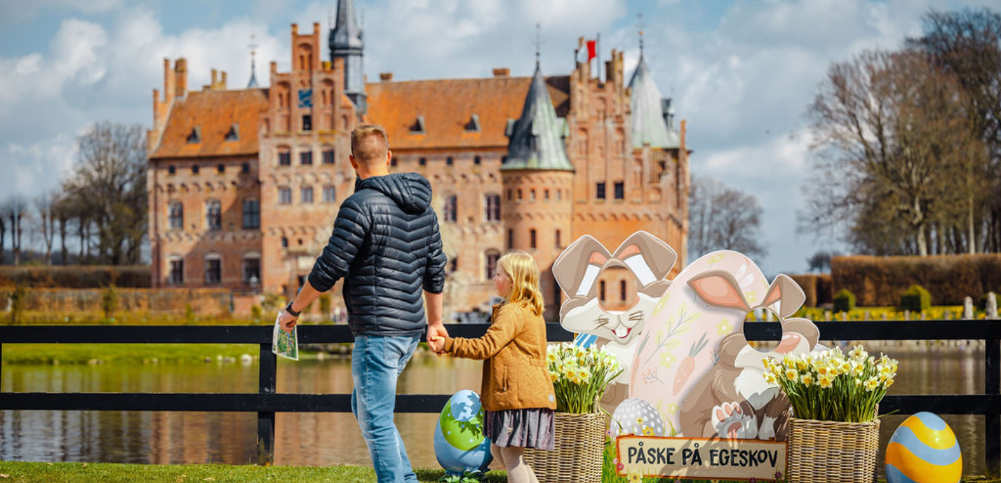 En far og datter går hånd i hånd med Egeskov Slot i baggrunden, og med påskedekoration omkring sig.
