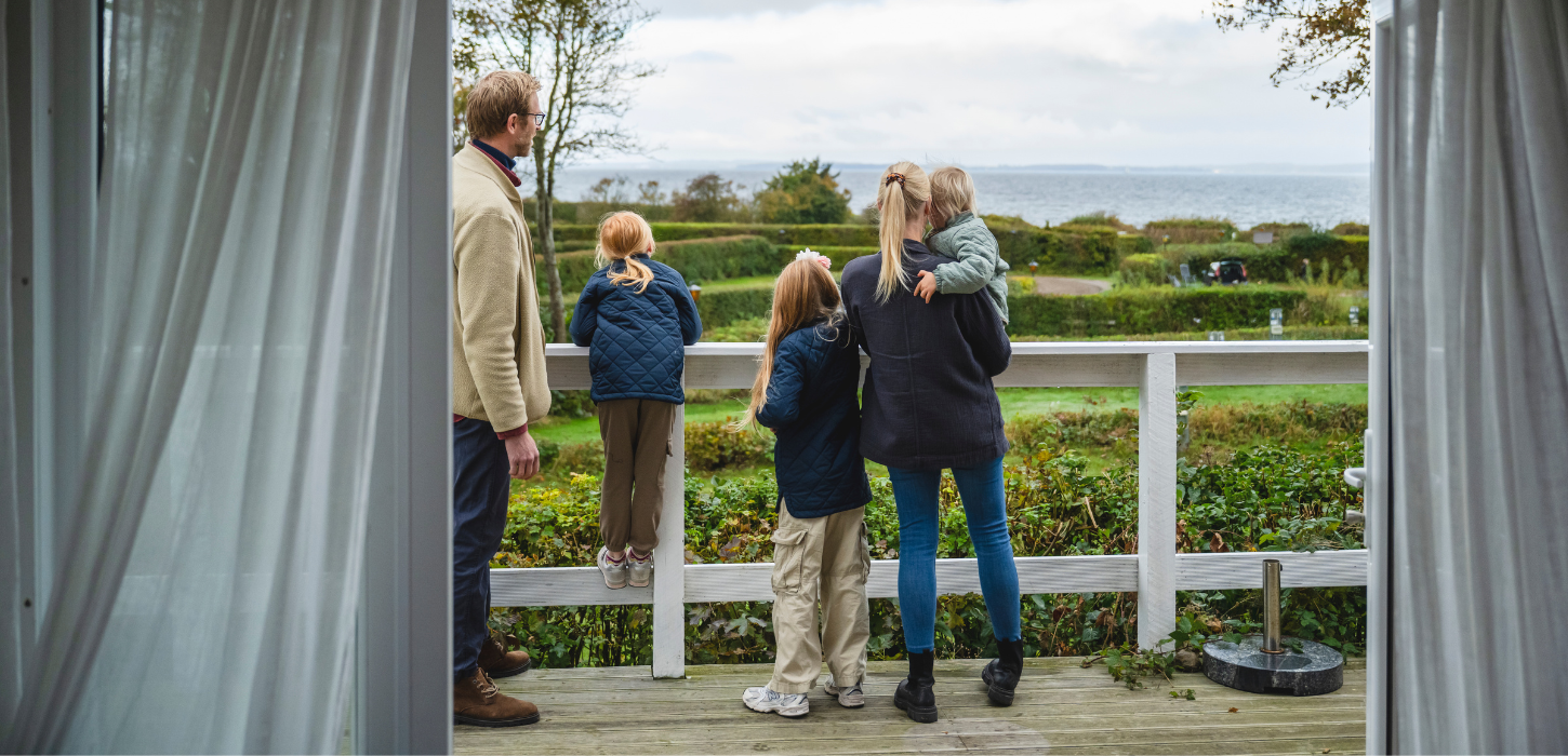 Familie på fem står med ryggen til og ser ud over campingplads og havet.