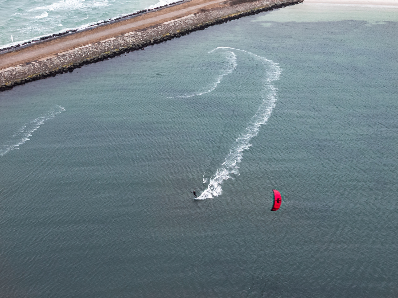 En kitesurfer med rødt sejl driver på stille vand ud for en dæmning